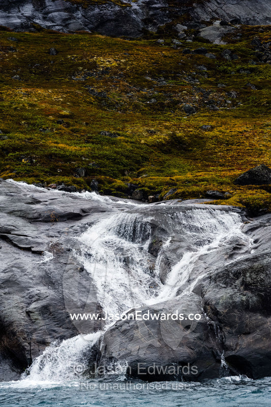 A freshwater stream cascades down a mountainside in an Arctic fjord. Fjord of Eternity, Maniitsoq, Sukkertoppen, Qeqqata Municipality, Greenland.
