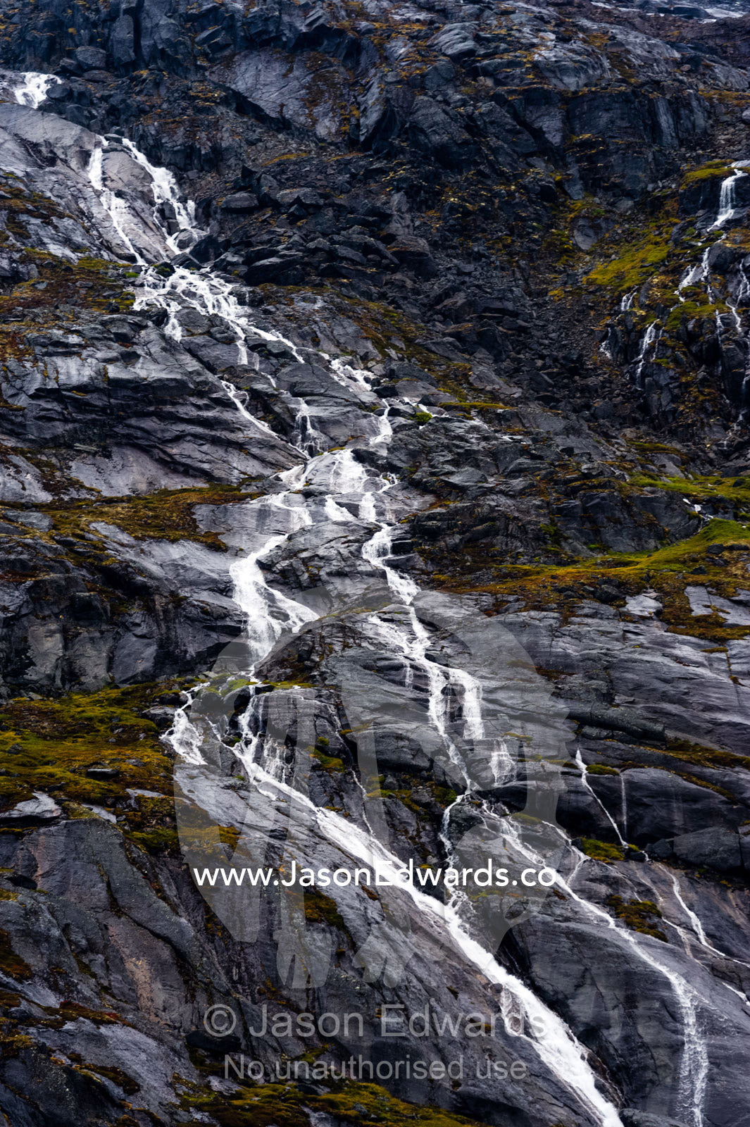A freshwater stream cascades down a mountainside in an Arctic fjord. Fjord of Eternity, Maniitsoq, Sukkertoppen, Qeqqata Municipality, Greenland.