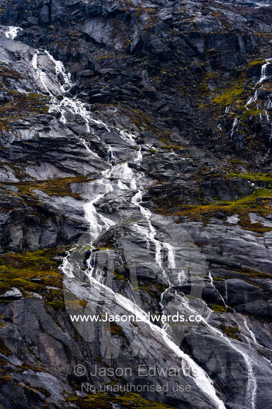 A freshwater stream cascades down a mountainside in an Arctic fjord. Fjord of Eternity, Maniitsoq, Sukkertoppen, Qeqqata Municipality, Greenland.