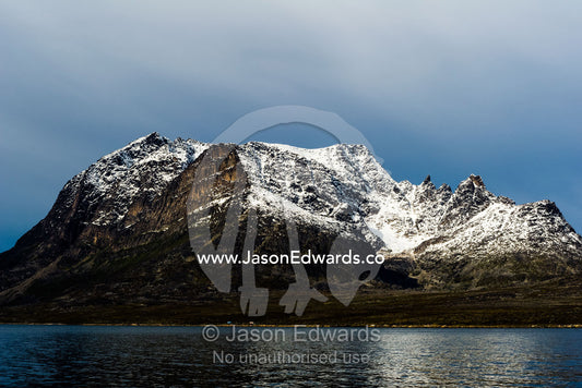 Snow covered peaks cast a pale light on the dark waters of a fjord. Davis Strait, Kangaamiut, Gammel Sukkertoppen, Qeqqata Municipality, Greenland.
