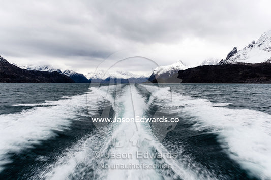 A boats wake peels between snow covered peaks in a fjord. Fjord of Eternity, Maniitsoq, Sukkertoppen, Qeqqata Municipality, Greenland.