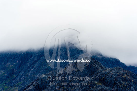 Clouds shroud the summit of a barren mountain range. Davis Strait, Fjord of Eternity, Maniitsoq, Sukkertoppen, Qeqqata Municipality, Greenland.