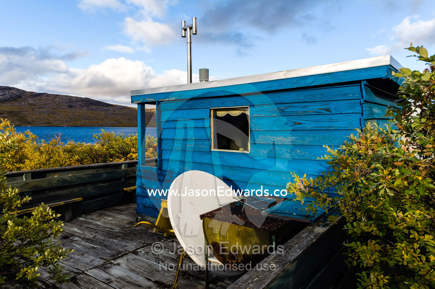 A satellite dish resting against the wall of a lakeside cottage closed for the winter. Tasersuatsiaq Lake, Kangerlussuaq, Qeqqata Municipality, Greenland.