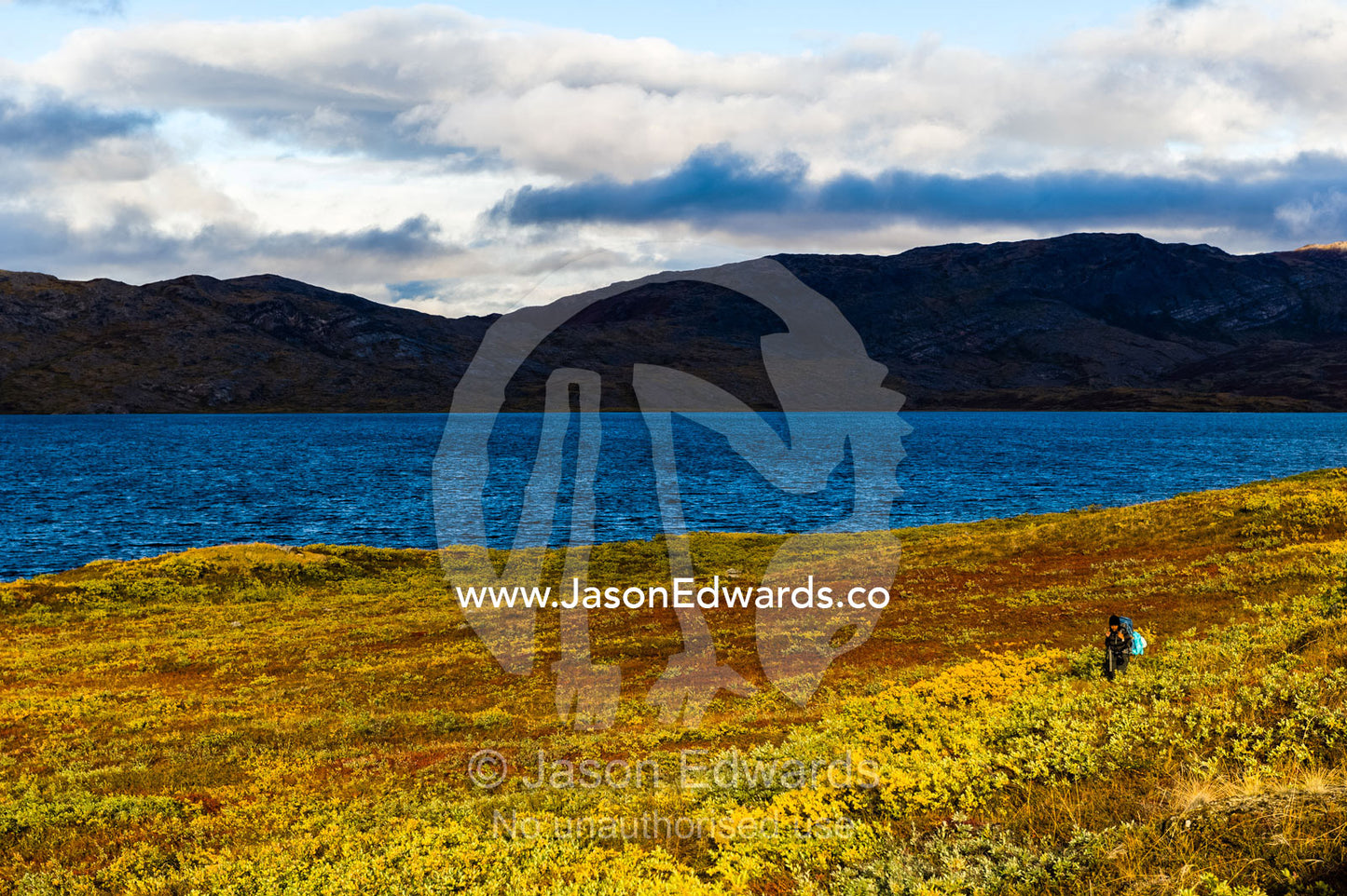 A solitary hiker on the shores of a vast alpine lake. Tasersuatsiaq Lake, Kangerlussuaq, Qeqqata Municipality, Greenland.