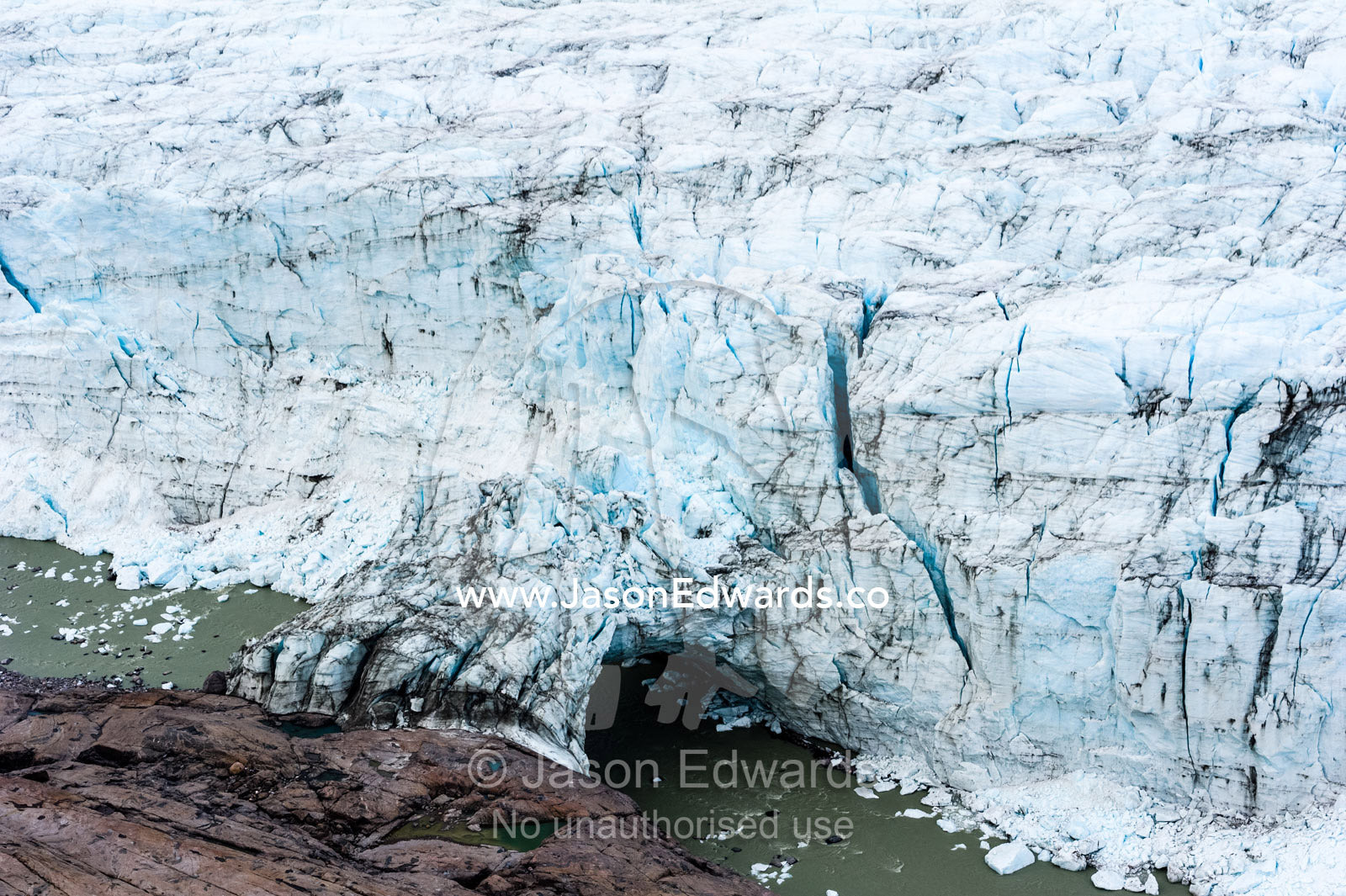 A river running beneath an ice bridge from a glacier fracture zone to the land. Russell Glacier, Greenland Ice Sheet, Qeqqata Municipality, Kangerlussuaq, Greenland.