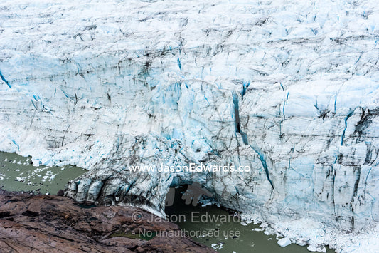 A river running beneath an ice bridge from a glacier fracture zone to the land. Russell Glacier, Greenland Ice Sheet, Qeqqata Municipality, Kangerlussuaq, Greenland.