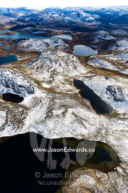 Snow-covered rocky mountaintops surround pristine alpine lakes on a highland tundra. Tarajornitsut Highlands, Qeqqata Municipality, Kangerlussuaq, Greenland.