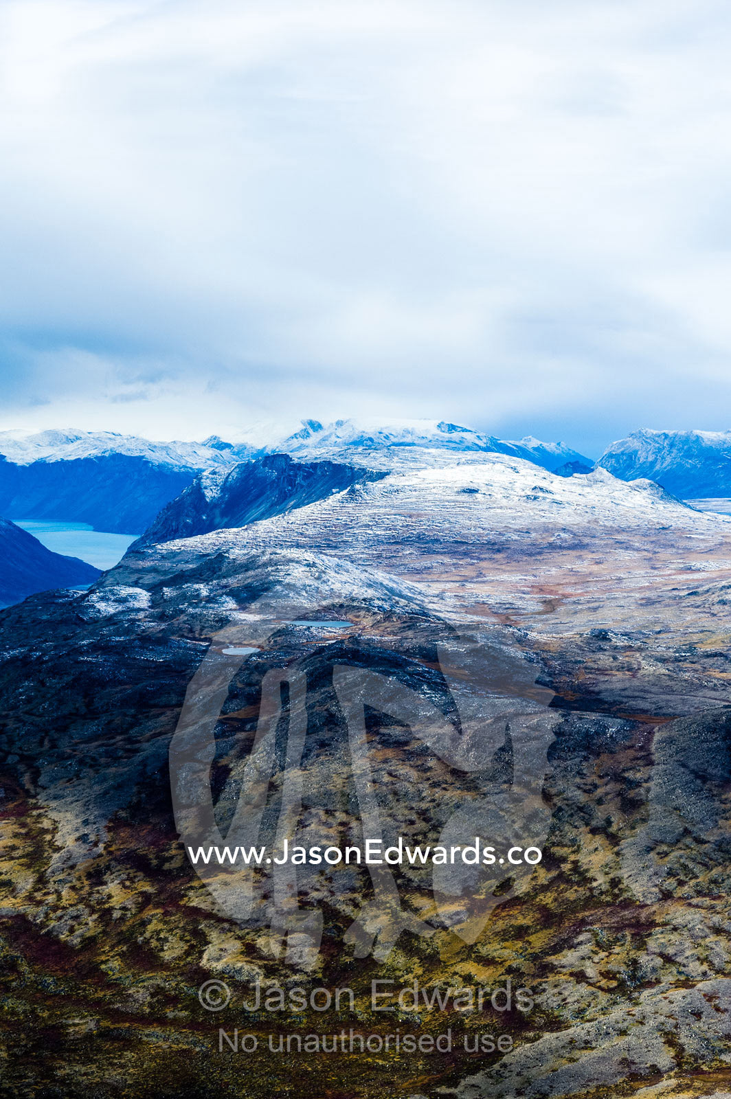 A dusting of snow covers mountain peaks on a highland tundra plateau. Tarajornitsut Highlands, Qeqqata Municipality, Kangerlussuaq, Greenland.