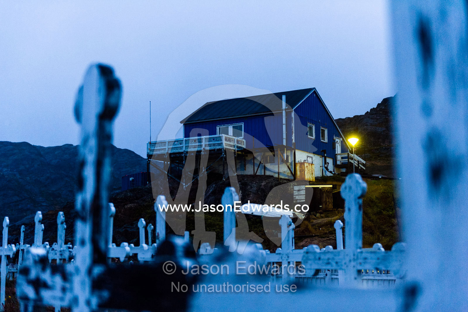 Nightfall over the grave tombstones and crucifix in a fishing village cemetery. Maniitsoq, Sukkertoppen, Qeqqata Municipality, Greenland.