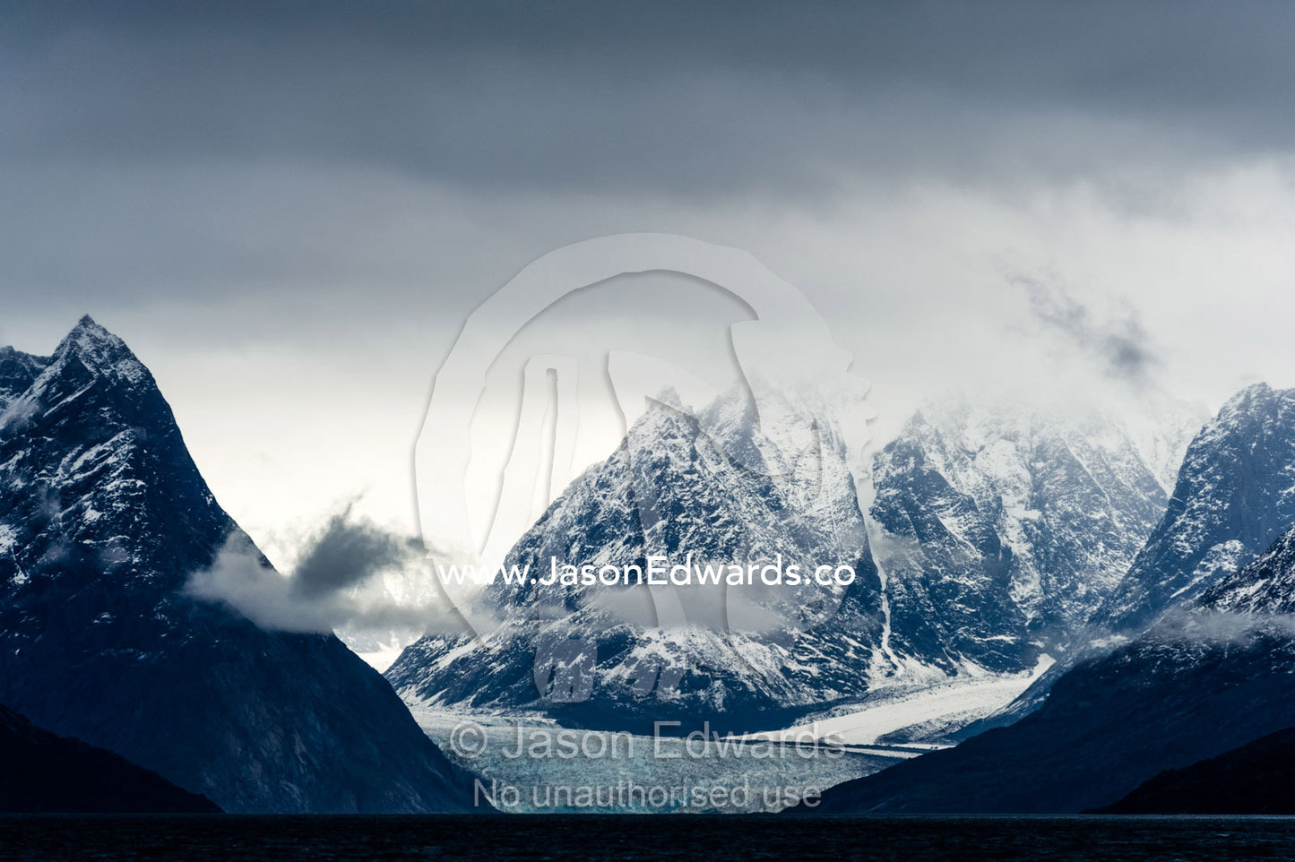 Jagged mountain peaks rise above a glacier in a arctic fjord. Fjord of Eternity, Maniitsoq, Sukkertoppen, Qeqqata Municipality, Greenland.