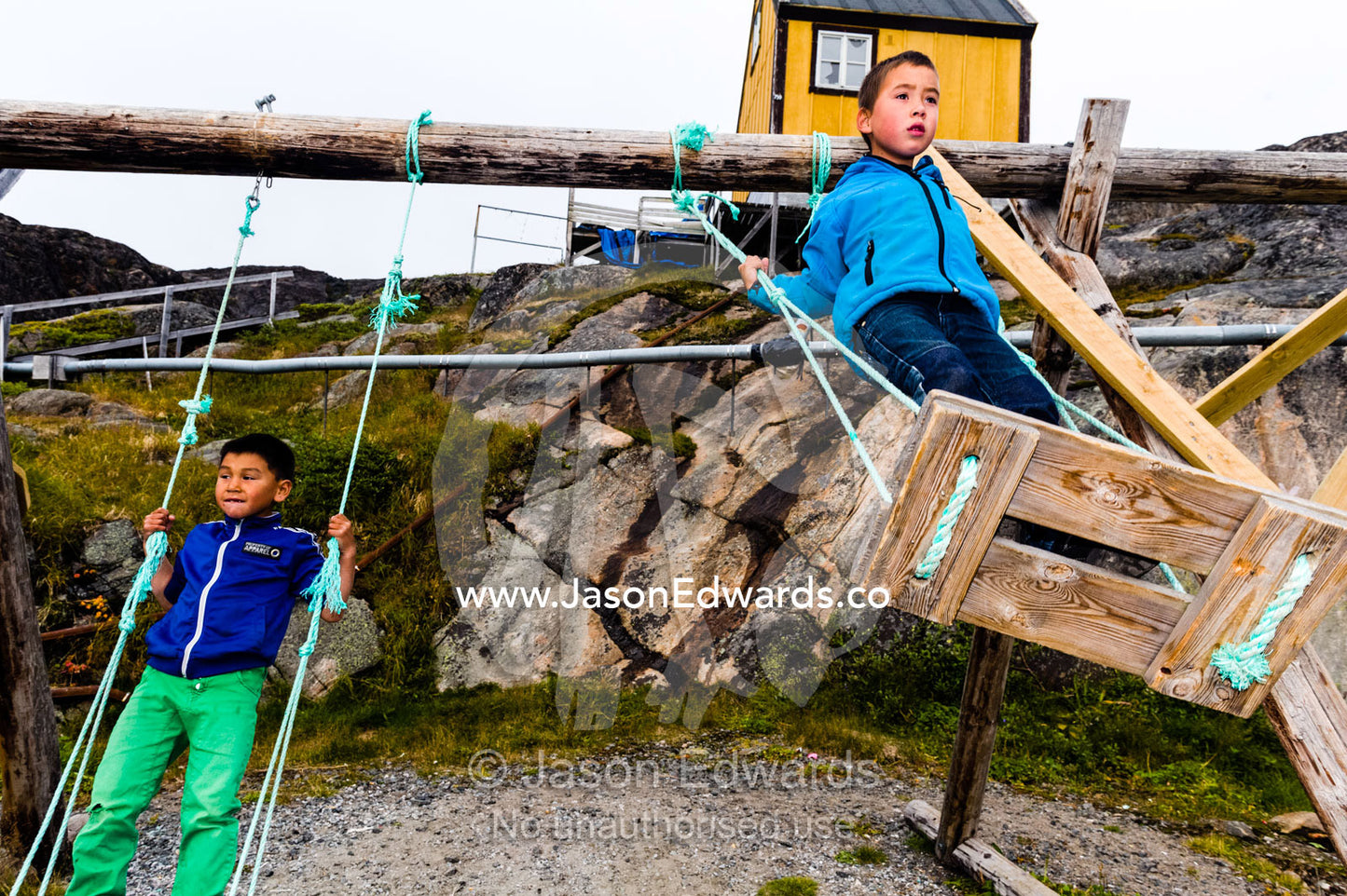Boys playing on swings in a village playground on an arctic island. Kangaamiut, Gammel Sukkertoppen, Qeqqata Municipality, Greenland.