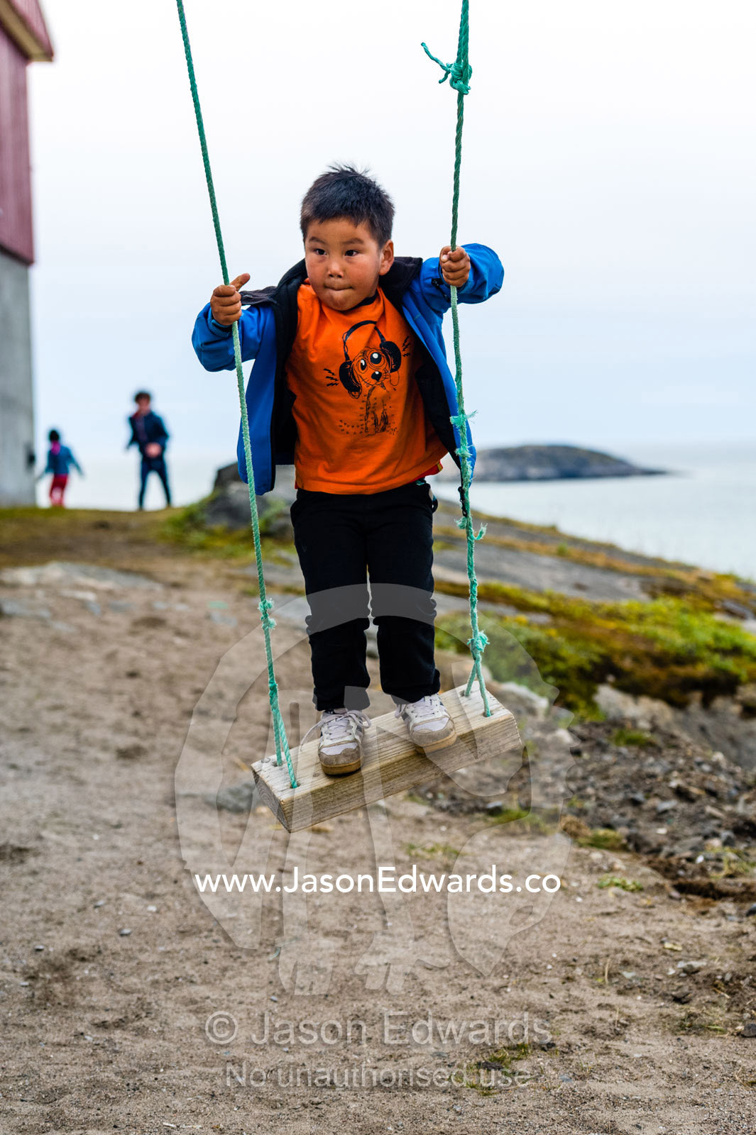 A boy playing on a rope swing in an arctic village. Kangaamiut, Gammel Sukkertoppen, Qeqqata Municipality, Greenland.