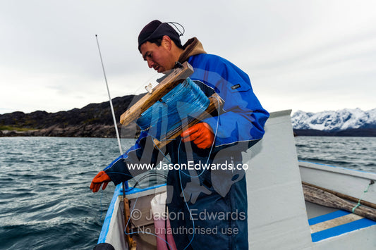An arctic fisherman fishing from a boat in a fiord. Davis Strait, Kangaamiut, Gammel Sukkertoppen, Qeqqata Municipality, Greenland.