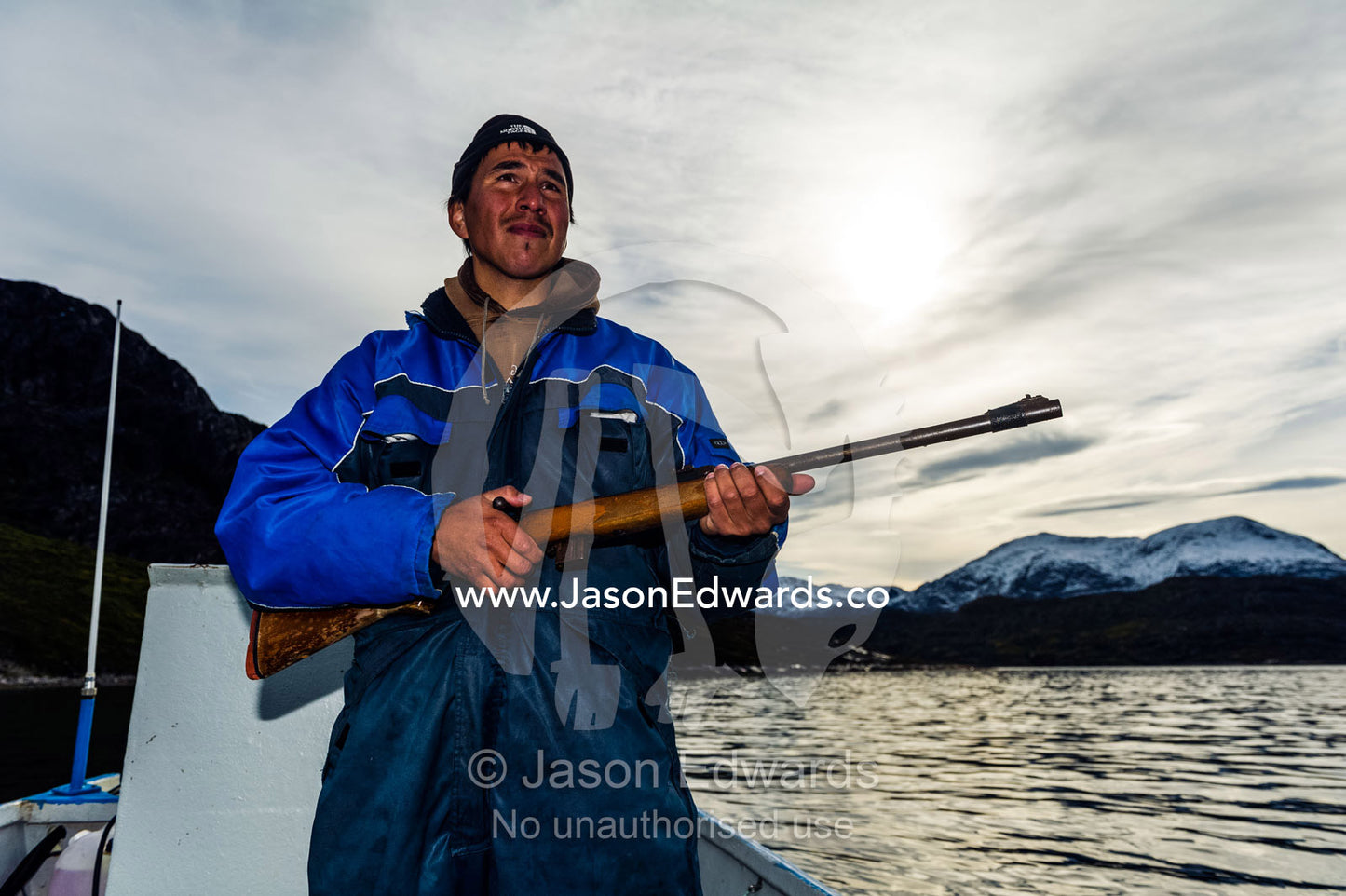 An arctic hunter with a rifle searching for seals from a boat in a fiord. Davis Strait, Kangaamiut, Gammel Sukkertoppen, Qeqqata Municipality, Greenland.