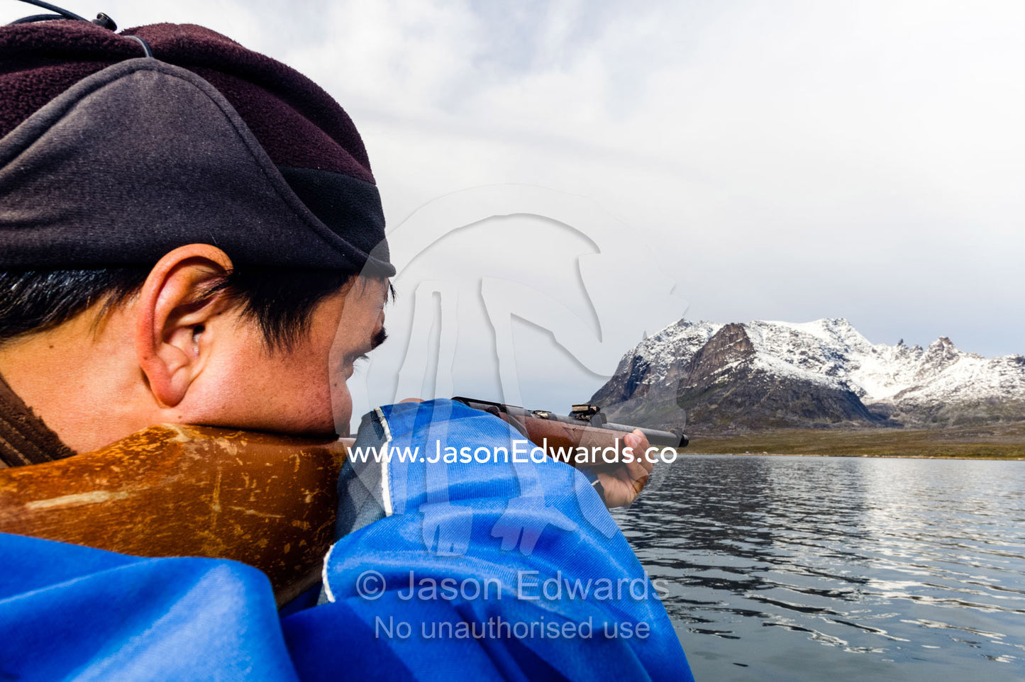 An arctic hunter with a rifle searching for seals from a boat in a fiord. Davis Strait, Kangaamiut, Gammel Sukkertoppen, Qeqqata Municipality, Greenland.