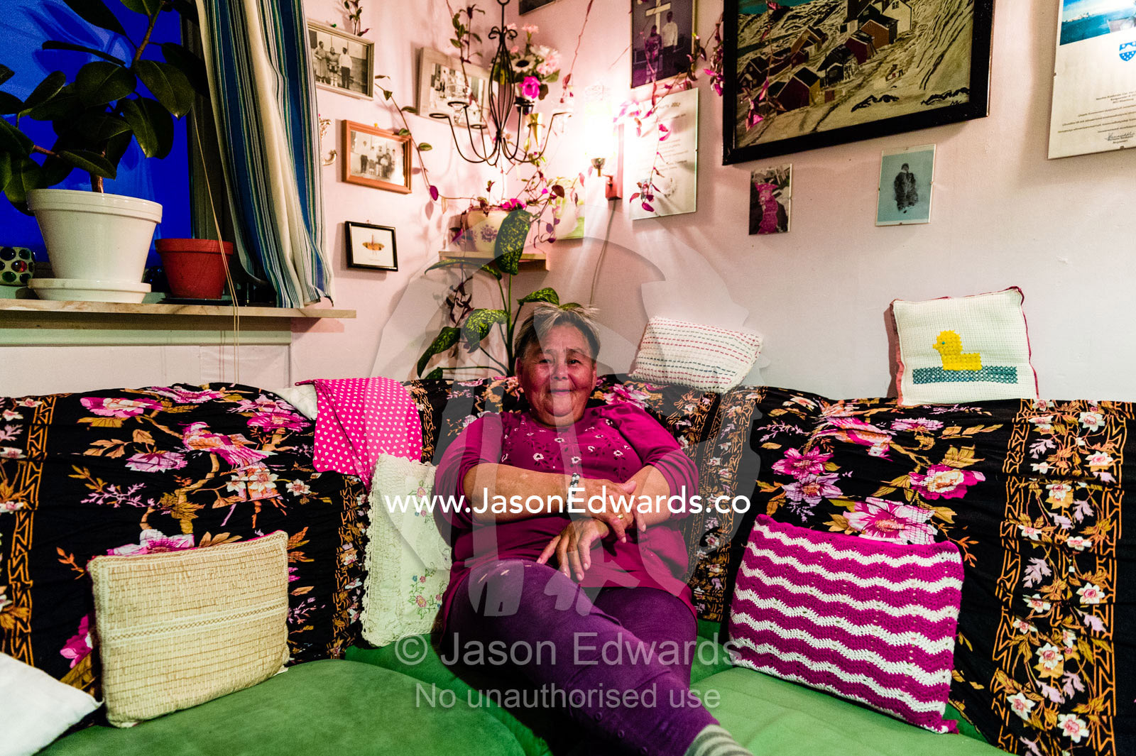 A woman relaxes on her sofa in the cozy warmth of her home on an arctic island. Kangaamiut, Gammel Sukkertoppen, Qeqqata Municipality, Greenland.