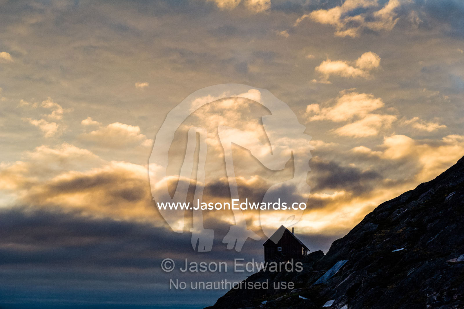 The silhouette of a cottage perched on a rocky outcrop on an arctic island. Kangaamiut, Gammel Sukkertoppen, Qeqqata Municipality, Greenland.