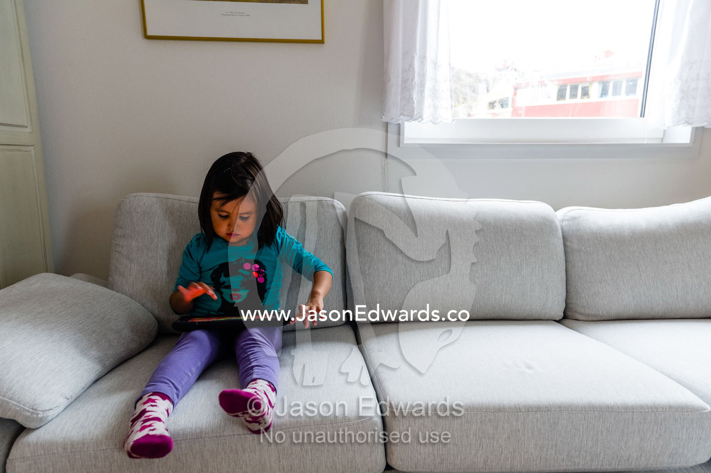 A small girl playing on an electronic tablet in an arctic village home. Kangaamiut, Gammel Sukkertoppen, Qeqqata Municipality, Greenland.