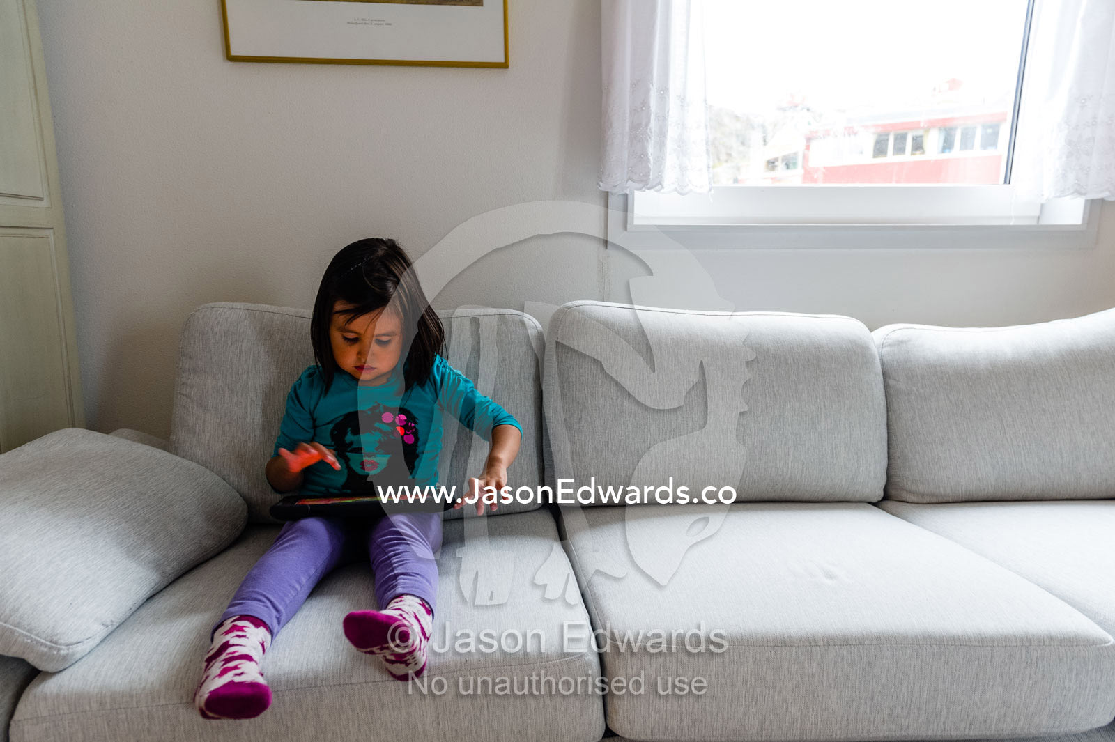 A small girl playing on an electronic tablet in an arctic village home. Kangaamiut, Gammel Sukkertoppen, Qeqqata Municipality, Greenland.