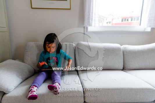 A small girl playing on an electronic tablet in an arctic village home. Kangaamiut, Gammel Sukkertoppen, Qeqqata Municipality, Greenland.