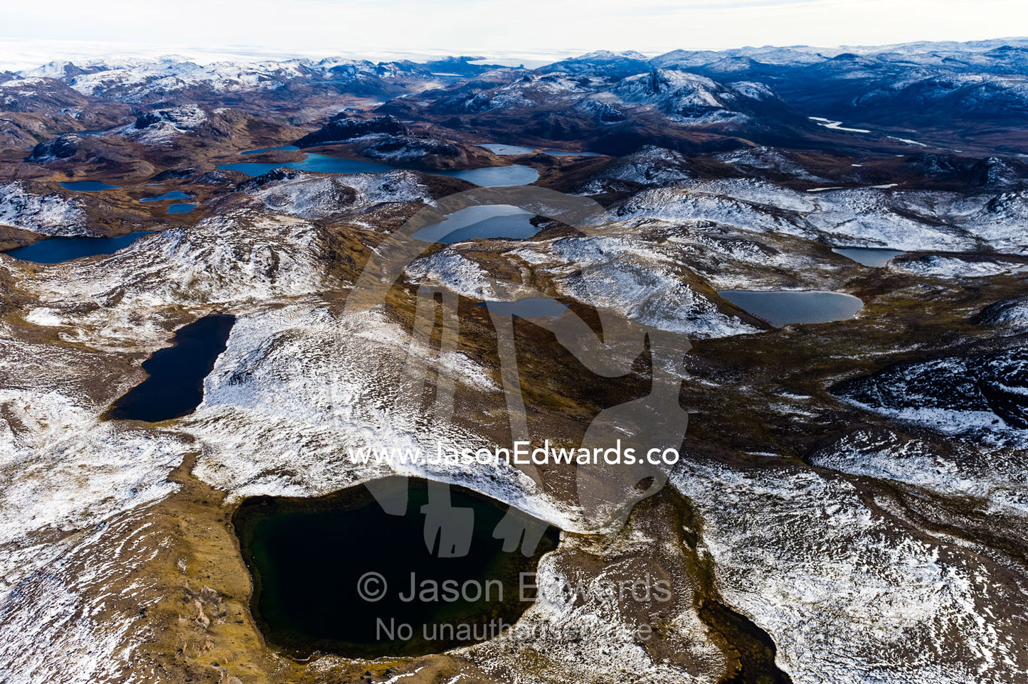Snow-covered rocky mountains surround pristine alpine lakes on a highland tundra. Tarajornitsut Highlands, Qeqqata Municipality, Kangerlussuaq, Greenland.