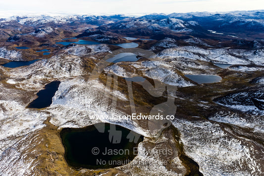 Snow-covered rocky mountains surround pristine alpine lakes on a highland tundra. Tarajornitsut Highlands, Qeqqata Municipality, Kangerlussuaq, Greenland.