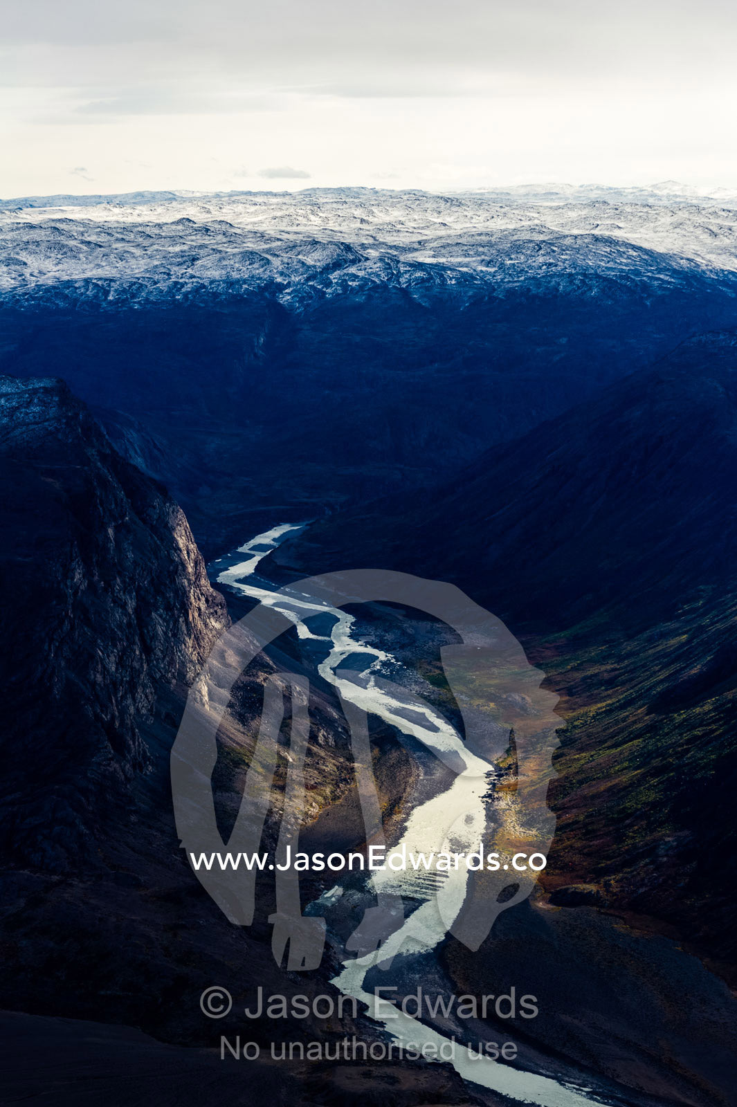 A winding river snakes its way through a highland tundra valley between steep mountains. Tarajornitsut Highlands, Qeqqata Municipality, Kangerlussuaq, Greenland.