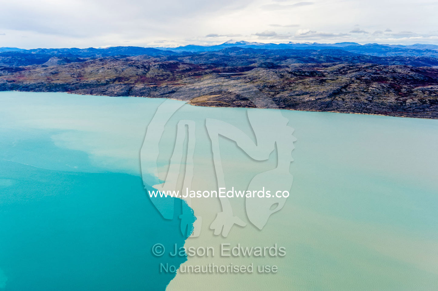 Silt from a river outwash plain stains the blue water of a fjord. Davis Strait, Kangerlussuaq Fjord, Kangerlussuaq, Qeqqata Municipality, Greenland.