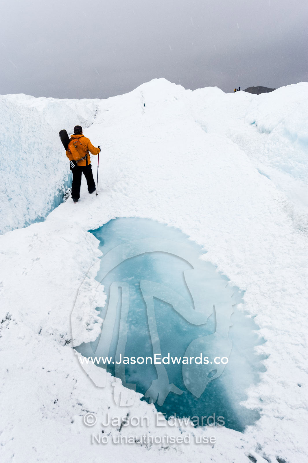A hiker passing between a dangerous crevasse and a melt pond on the Greenland Ice Shelf. Greenland Ice Sheet, Qeqqata Municipality, Kangerlussuaq, Greenland.