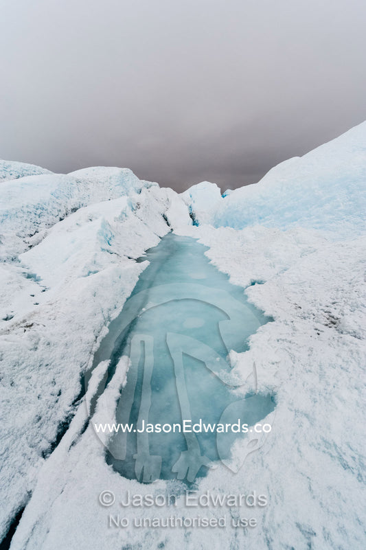 The blue frozen surface of a melt pond on the Greenland Ice Shelf. Greenland Ice Sheet, Qeqqata Municipality, Kangerlussuaq, Greenland.