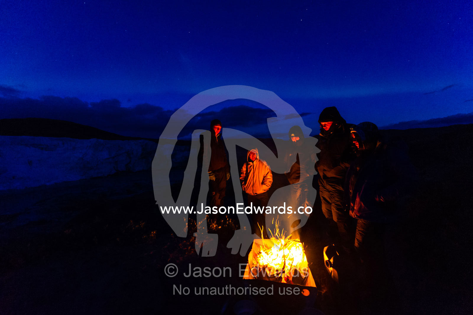 Hikers surround a fire to get warm whilst camping at the base of a glacier. Russell Glacier, Greenland Ice Sheet, Qeqqata Municipality, Kangerlussuaq, Greenland.