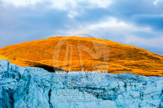 Sunset turns the exposed summit of a mountain orange above a glacier fracture zone. Russell Glacier, Greenland Ice Sheet, Qeqqata Municipality, Kangerlussuaq, Greenland.