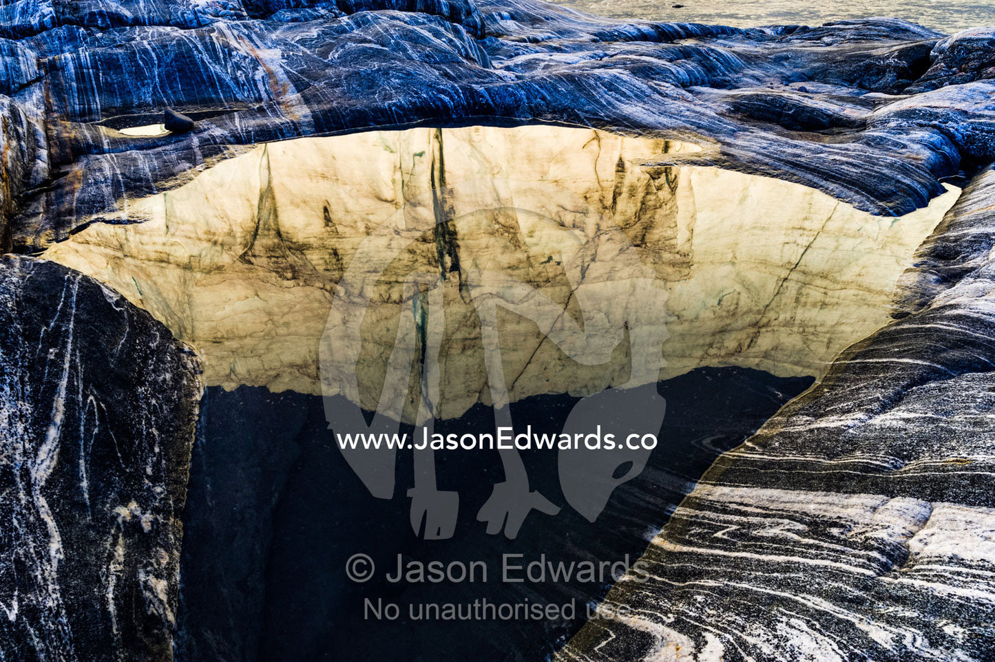 The setting sun reflects the sheer ice cliff of a glacier fracture zone in a pond. Russell Glacier, Greenland Ice Sheet, Qeqqata Municipality, Kangerlussuaq, Greenland.