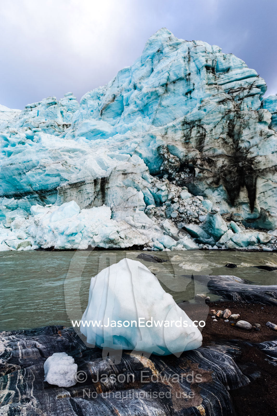 A block of ice carved from a glacier resting by a river. Qinnguata Kuussua River, Russell Glacier, Greenland Ice Sheet, Qeqqata Municipality, Kangerlussuaq, Greenland.