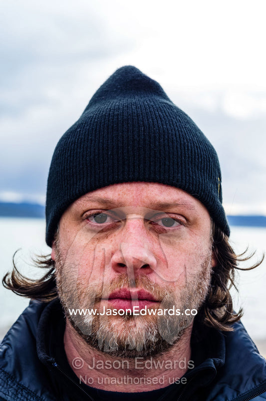 A tired man wearing a woolen beanie on an arctic fiord. Kangerlussuaq Port, Kangerlussuaq Fjord, Kangerlussuaq, Qeqqata Municipality, Greenland.