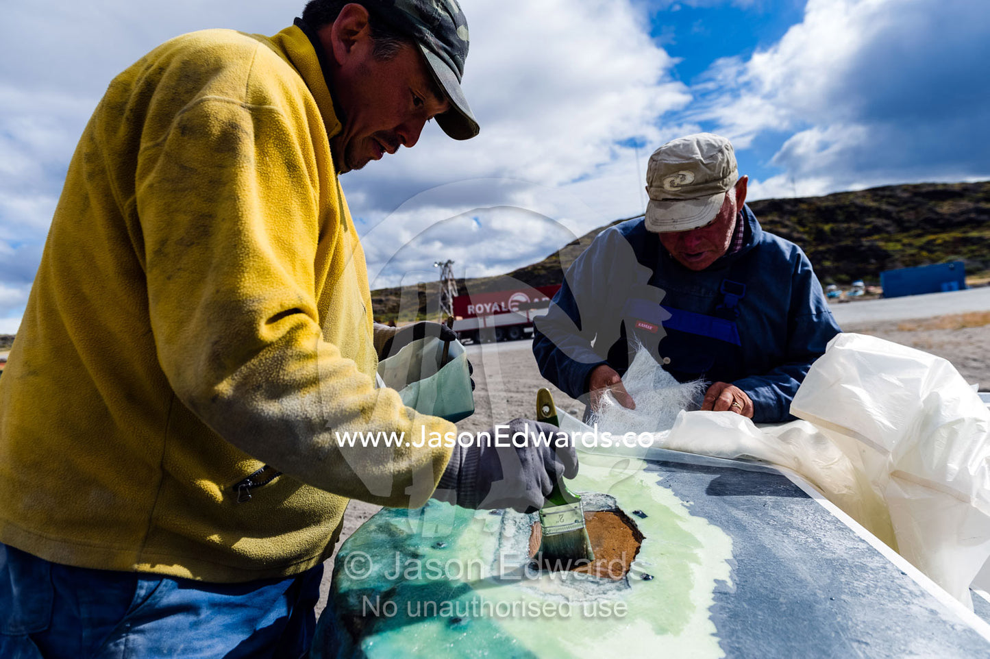 Fishermen repairing a boat with fiberglass sheets and resin. Kangerlussuaq Port, Kangerlussuaq Fjord, Kangerlussuaq, Qeqqata Municipality, Greenland.