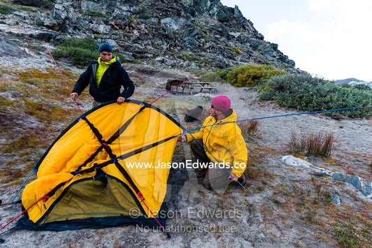 A Greenland guide assists a  tourist to set-up a tent on the windy tundra. Russell Glacier, Greenland Ice Sheet, Qeqqata Municipality, Kangerlussuaq, Greenland.