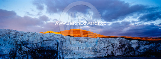 Sunset turns the exposed summit of a mountain orange above a glacier fracture zone. Russell Glacier, Greenland Ice Sheet, Qeqqata Municipality, Kangerlussuaq, Greenland.