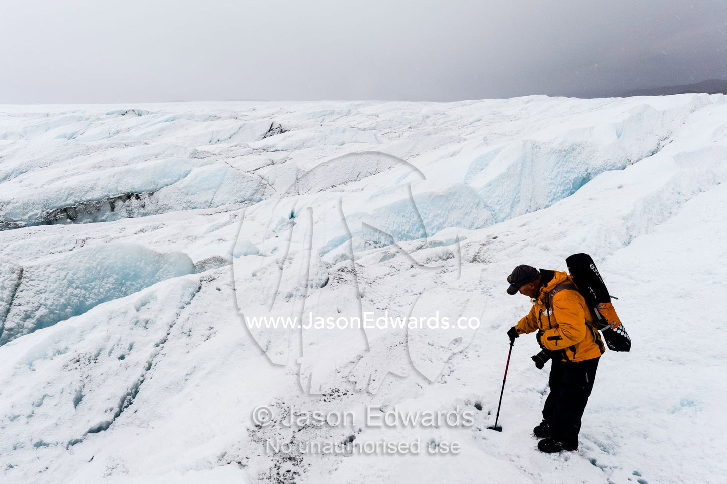 A hiker carefully tests the stability along the edge of a crevasse on the Greenland Ice Sheet. Greenland Ice Sheet, Qeqqata Municipality, Kangerlussuaq, Greenland.