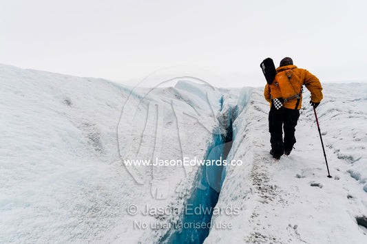 A hiker walks carefully along the edge of a crevasse on the Greenland Ice Sheet. Greenland Ice Sheet, Qeqqata Municipality, Kangerlussuaq, Greenland.