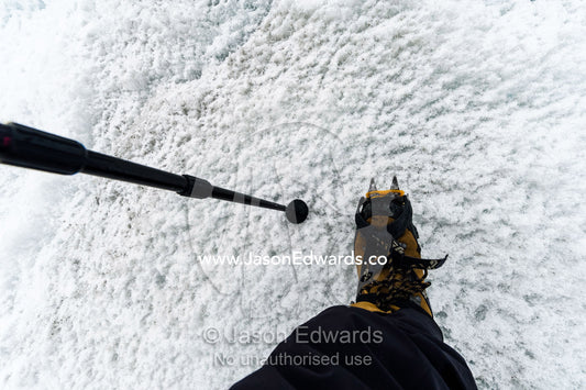A walking stick and hiking boots with crampons spiking into the ice. Greenland Ice Sheet, Qeqqata Municipality, Kangerlussuaq, Greenland.