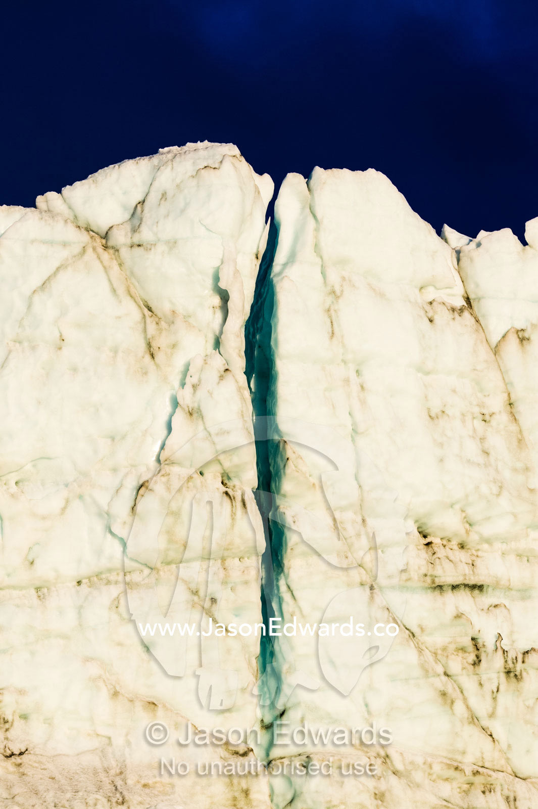 The setting sun illuminates a crevasse in the sheer ice cliff of a glacier fracture zone. Russell Glacier, Greenland Ice Sheet, Qeqqata Municipality, Kangerlussuaq, Greenland.