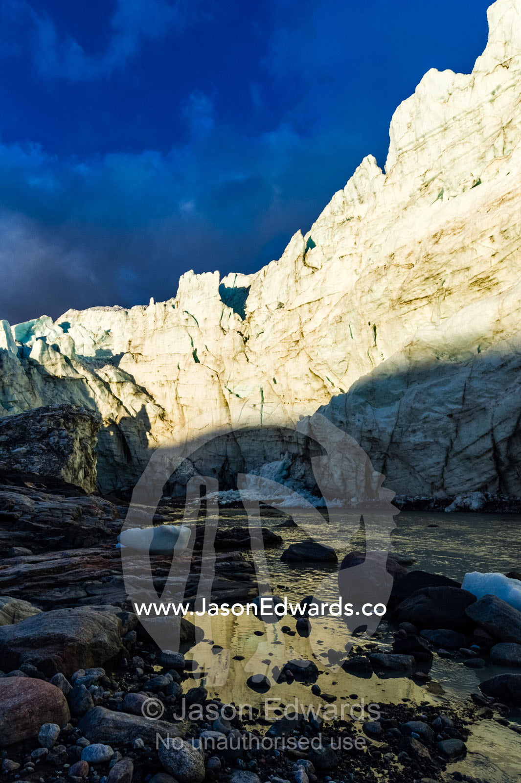 The setting sun illuminates the sheer ice cliff of a glacier fracture zone with a river at it's base. Qinnguata Kuussua River, Russell Glacier, Greenland Ice Sheet, Qeqqata Municipality, Kangerlussuaq, Greenland.