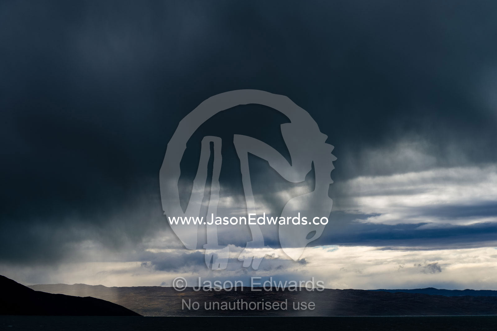 A rainstorm descends over a dark, grey ocean and fjord. Davis Strait, Kangerlussuaq Fjord, Kangerlussuaq, Qeqqata Municipality, Greenland.