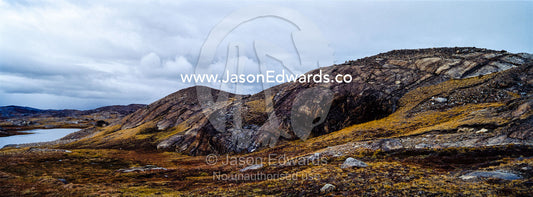 Outcrops of exposed barren rocks emerge through the tundra surrounding an alpine lake. Isunngua Highland, Kangerlussuaq, Qeqqata Municipality, Greenland.