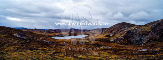 Outcrops of exposed barren rocks emerge through the tundra surrounding an alpine lake. Isunngua Highland, Kangerlussuaq, Qeqqata Municipality, Greenland.
