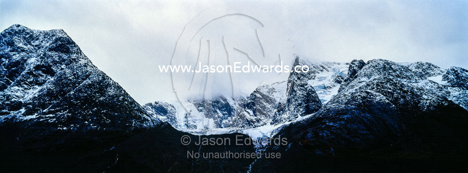 Rugged black mountain peaks shrouded in snow and ice tower above an arctic fjord. Fjord of Eternity, Maniitsoq, Sukkertoppen, Qeqqata Municipality, Greenland.