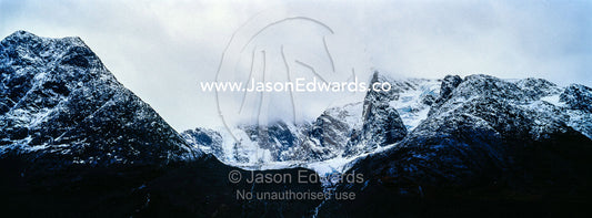 Rugged black mountain peaks shrouded in snow and ice tower above an arctic fjord. Fjord of Eternity, Maniitsoq, Sukkertoppen, Qeqqata Municipality, Greenland.