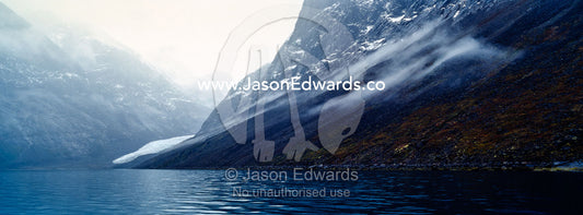 Mist clings to the slopes of a mountain in an Arctic fjord. Fjord of Eternity, Maniitsoq, Sukkertoppen, Qeqqata Municipality, Greenland.