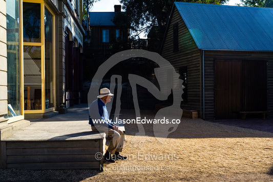 An elderly man rests on a porch whilst visiting a gold mine town museum. Sovereign Hill, Ballarat, Victoria, Australia.